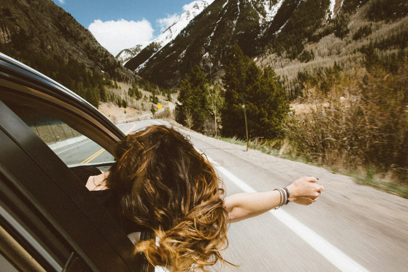 The car winds its way up the clear mountain road, climbing towards the sun-drenched peaks. With her hair flying in the wind, a girl leans out the window, waving her hand in the air—a perfect picture of freedom. This is the pure joy of a Morocco road trip, a moment of unforgettable adventure.