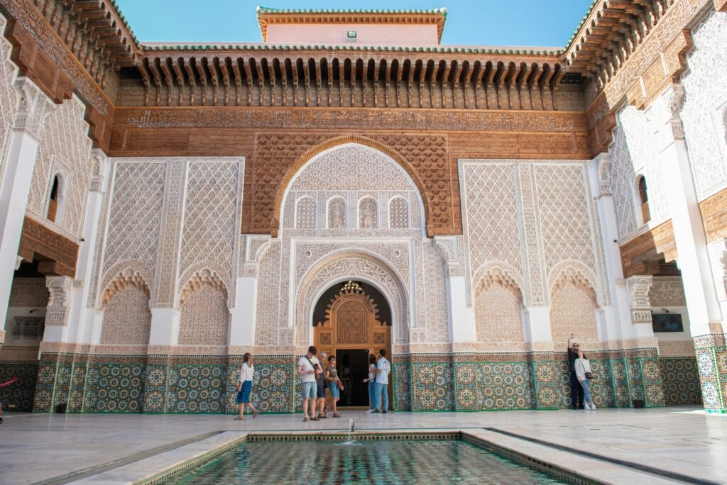 Moroccan hospitality This dynamic image shows visitors standing and exploring the grand atrium of a Luxury Riad Marrakech. They are admiring the stunning architectural details, from the high carved ceilings to the majestic arches, highlighting the space and luxury that defines this exceptional riad.