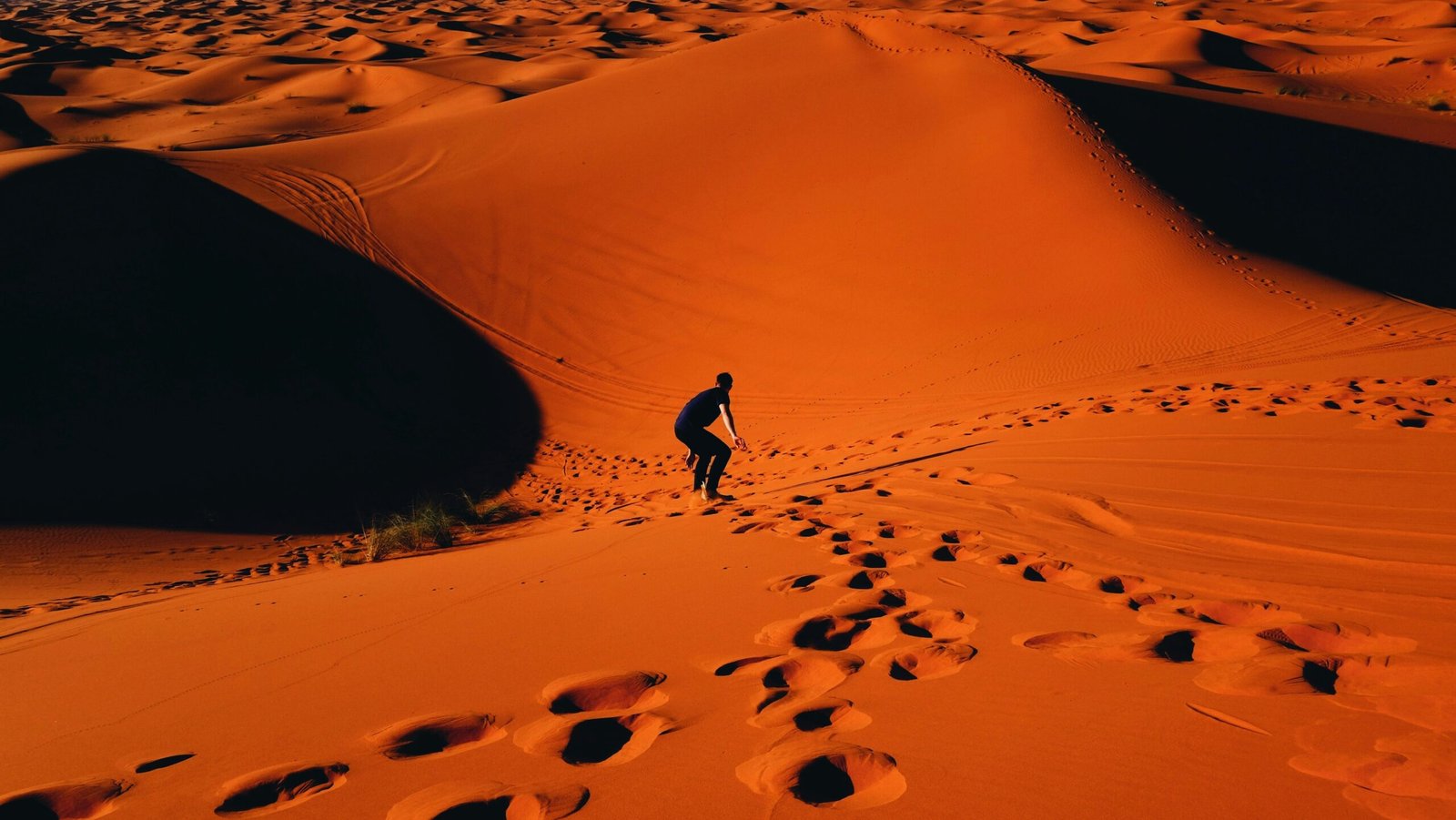 An adventurer skillfully sandboarding down golden dunes in the Moroccan desert Sandboarding Morocco, amidst a stunning landscape of wavy sands and clear skies.