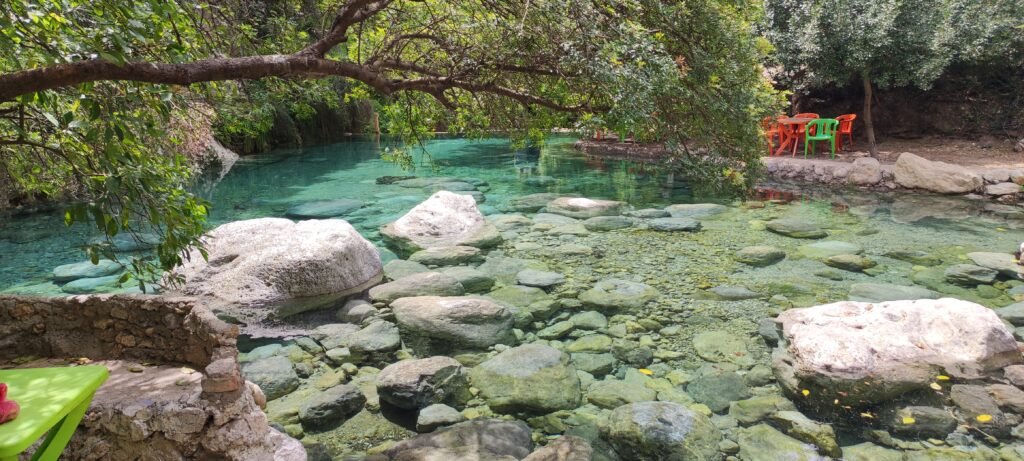 A stunning emerald pool nestled in the heart of the Akchour mountains, surrounded by lush rocks and greenery—a perfect serene stop during the Akchour waterfalls hike. The mountains reflect perfectly on the calm water, creating a breathtaking natural mirror.